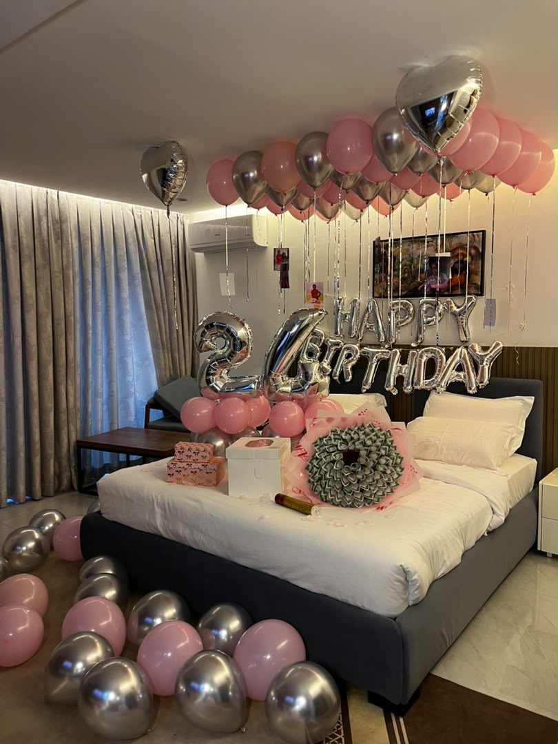 Bedroom birthday surprise setup with pink and silver balloons, foil letters and gifts on the bed