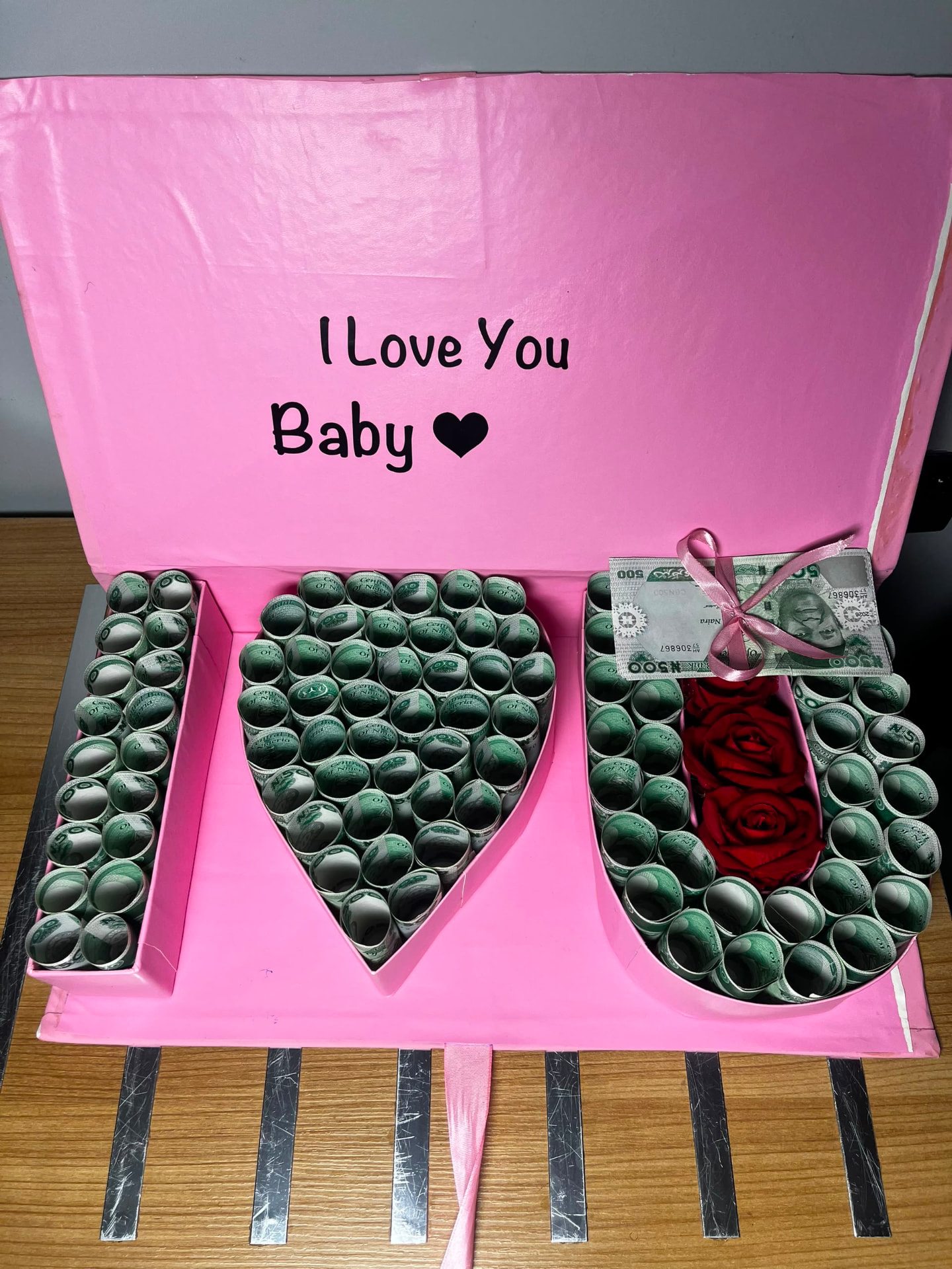 Pink money box with rolled naira notes shaped into a heart and preserved red roses